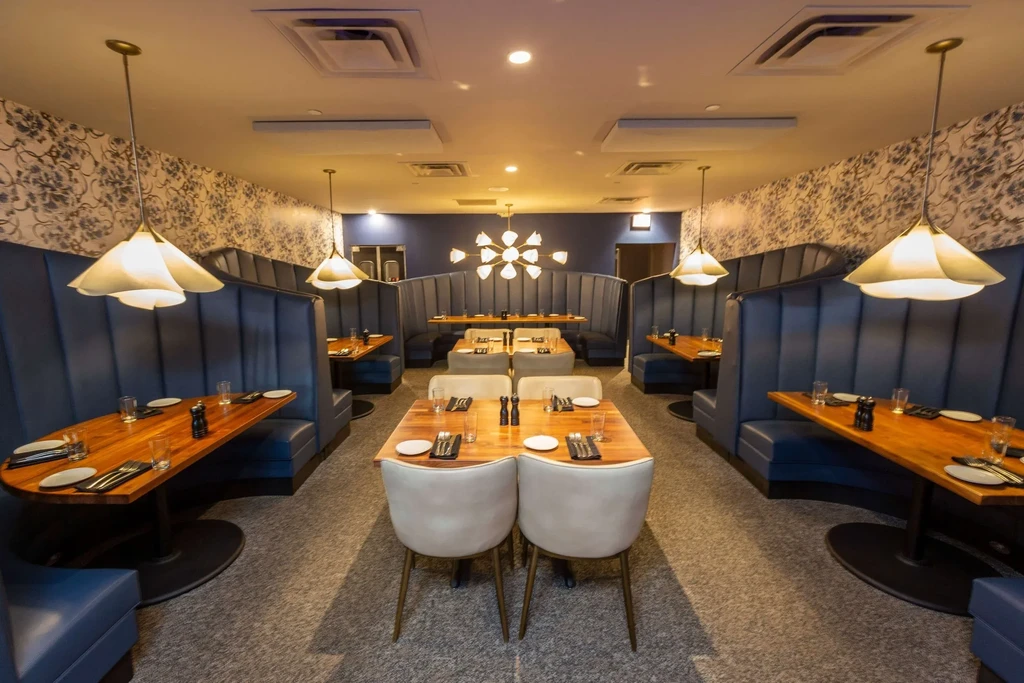 Modern restaurant interior with dark blue booths, wood tables, and chandeliers.