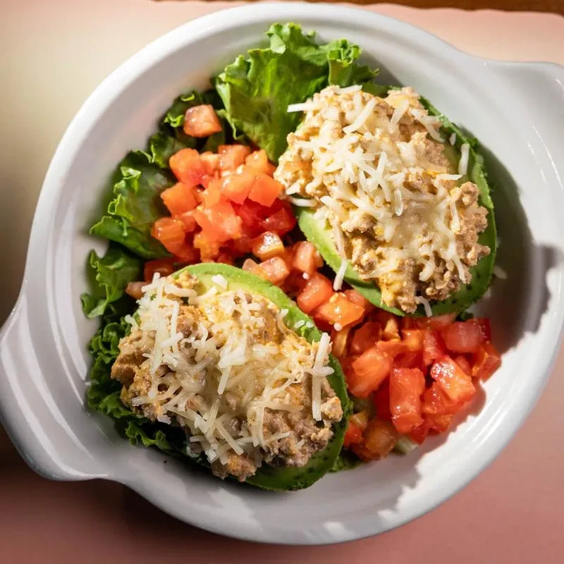 Two cheese-topped stuffed avocado halves with lettuce and tomatoes in a bowl.