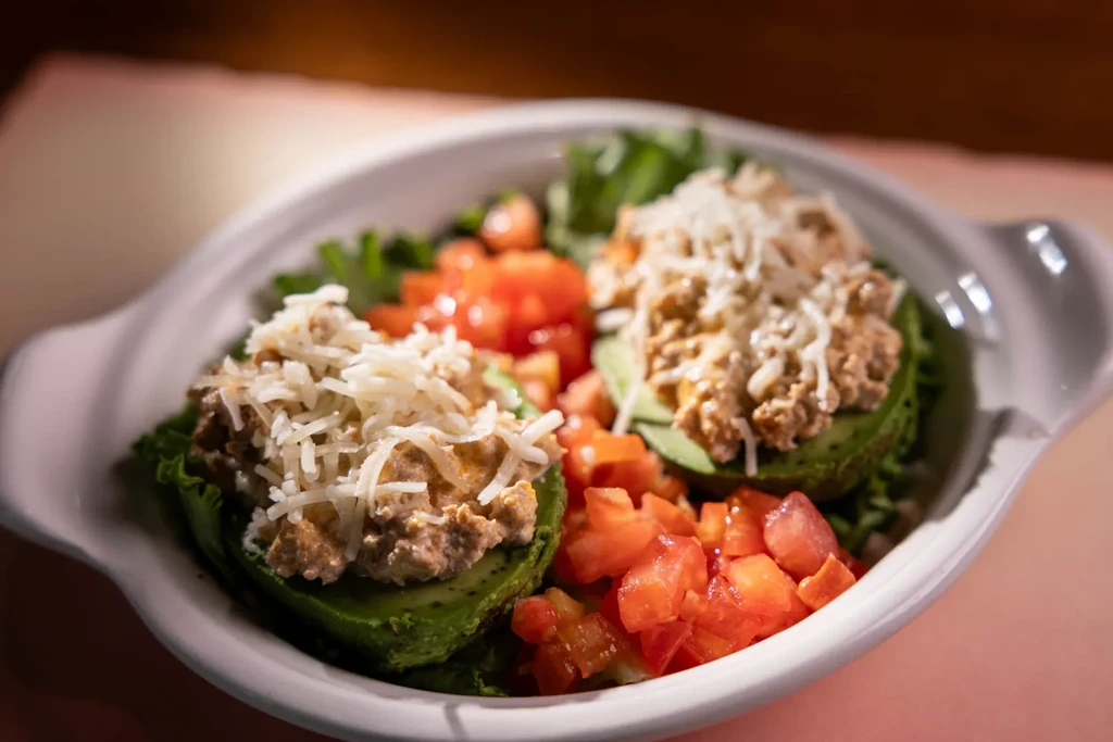 Avocado halves with creamy filling, cheese, lettuce, and diced tomatoes.