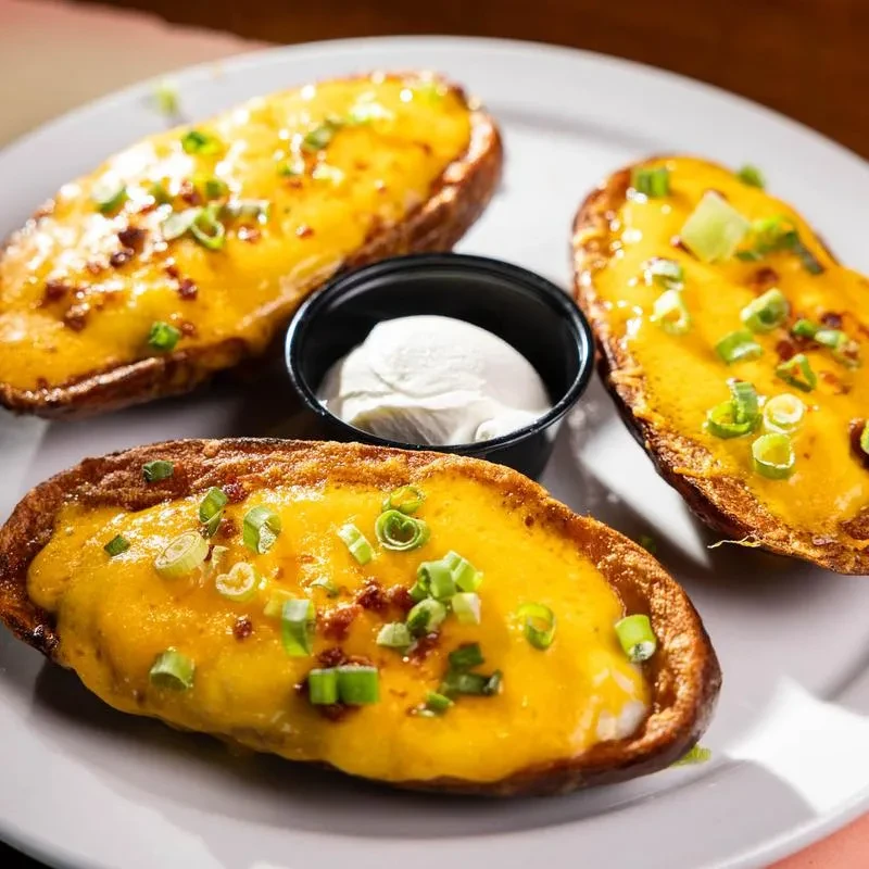 Three potato skins with cheese, bacon bits, green onions, and sour cream.