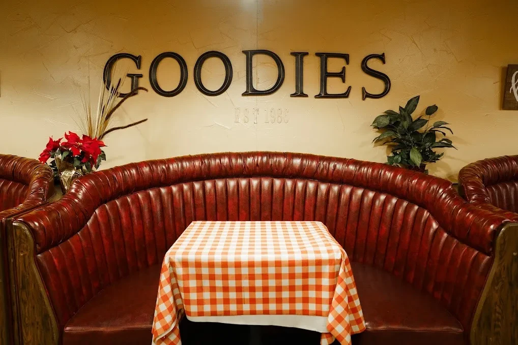 Classic restaurant booth with tufted reddish-brown leather, "GOODIES EST 1986" sign.