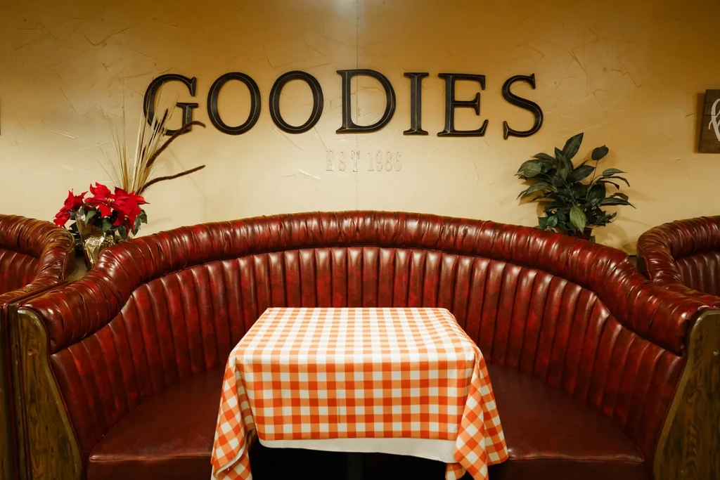 Red-brown tufted booth, checkered table, 'GOODIES EST 1986' wall sign.