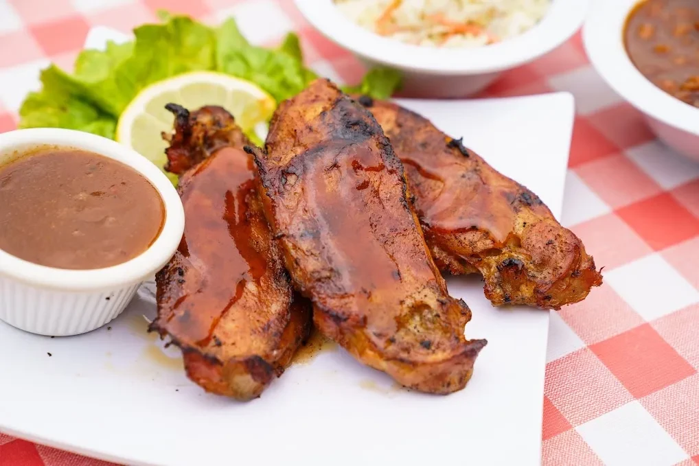 Grilled chicken, reddish-brown sauce, lemon, and sides on a checkered tablecloth.