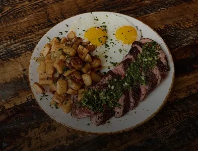 Steak, sunny-side-up eggs, and roasted potatoes with chimichurri on a table.