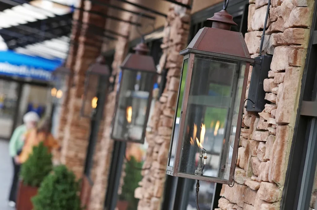 Row of outdoor gas lanterns with burning flames on a stone wall.