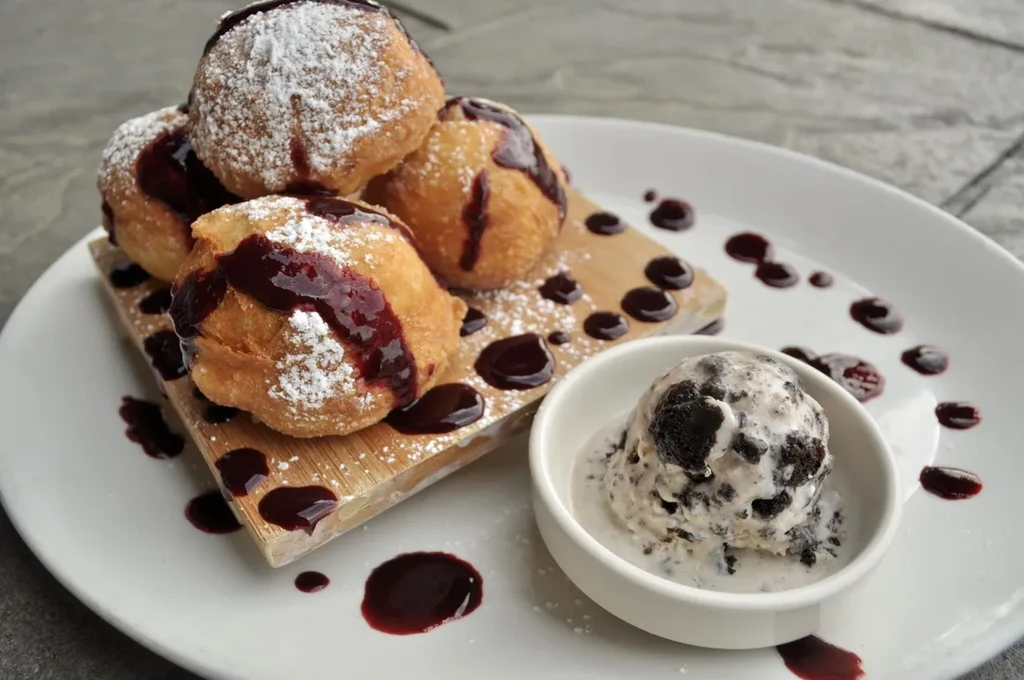 Stacked fried dough with powdered sugar, berry sauce, and cookies and cream ice cream.
