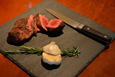 Sliced medium-rare steak, chef's knife, rosemary, and garlic on slate.