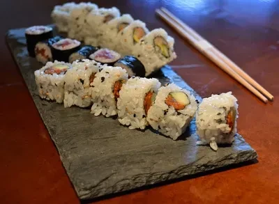 Assorted sushi rolls on dark slate platter with wooden chopsticks.