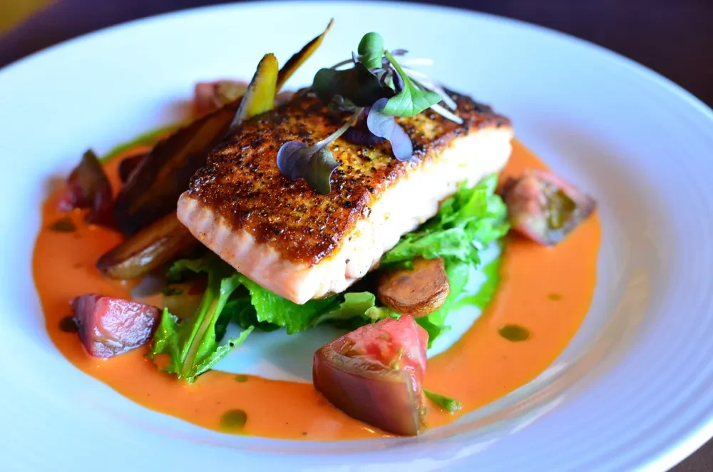 Plated seared salmon, crispy skin, roasted vegetables, tomato, creamy orange sauce.