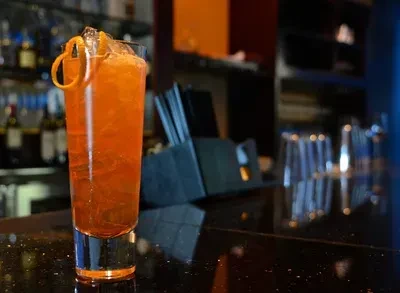 Vibrant orange cocktail with orange peel, ice on a dark bar.