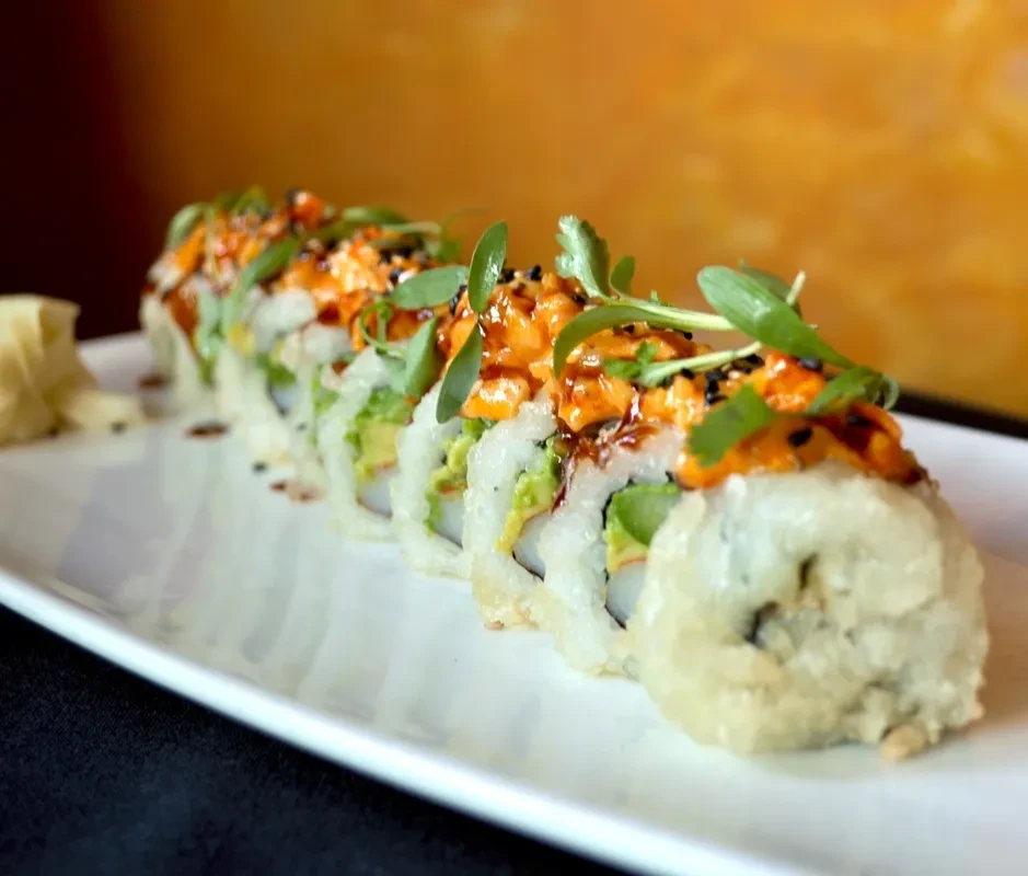 Seven sushi rolls with orange topping, microgreens, and pickled ginger.