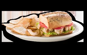 Grilled chicken hoagie with lettuce, tomato, and potato chips on a plate.