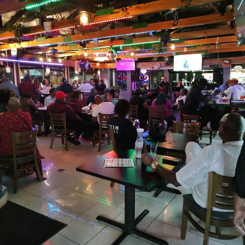 Crowded bar with live music, colorful lights, and visible TVs.