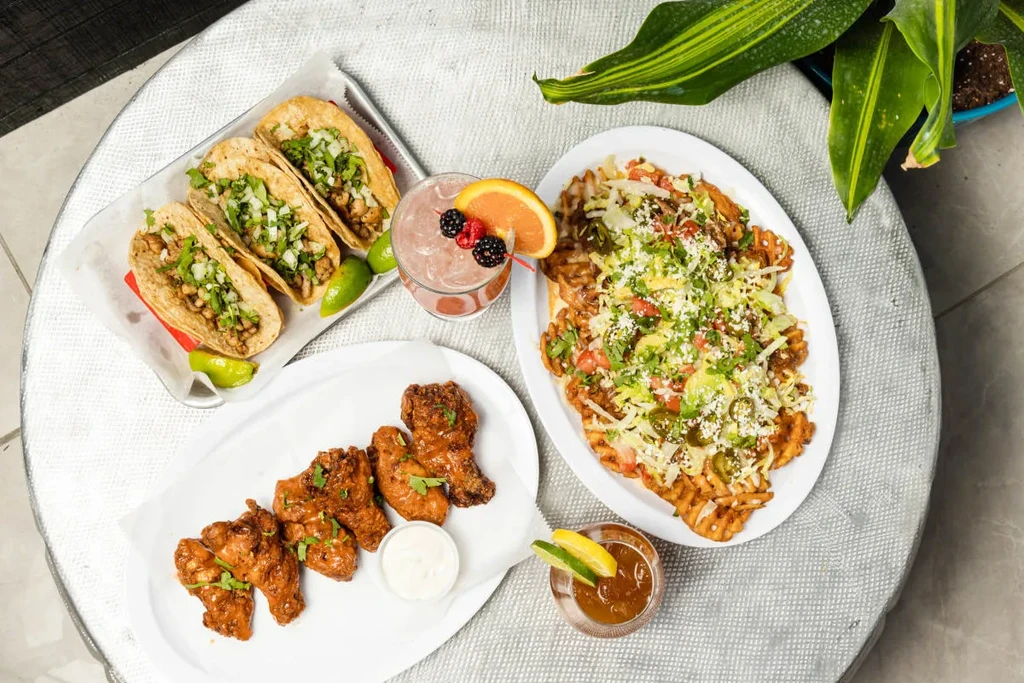 Overhead view of a table with tacos, wings, loaded fries, and cocktails.