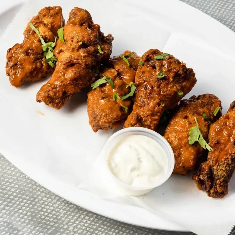 Crispy chicken wings with glossy reddish-brown sauce, green herbs, and dipping sauce.