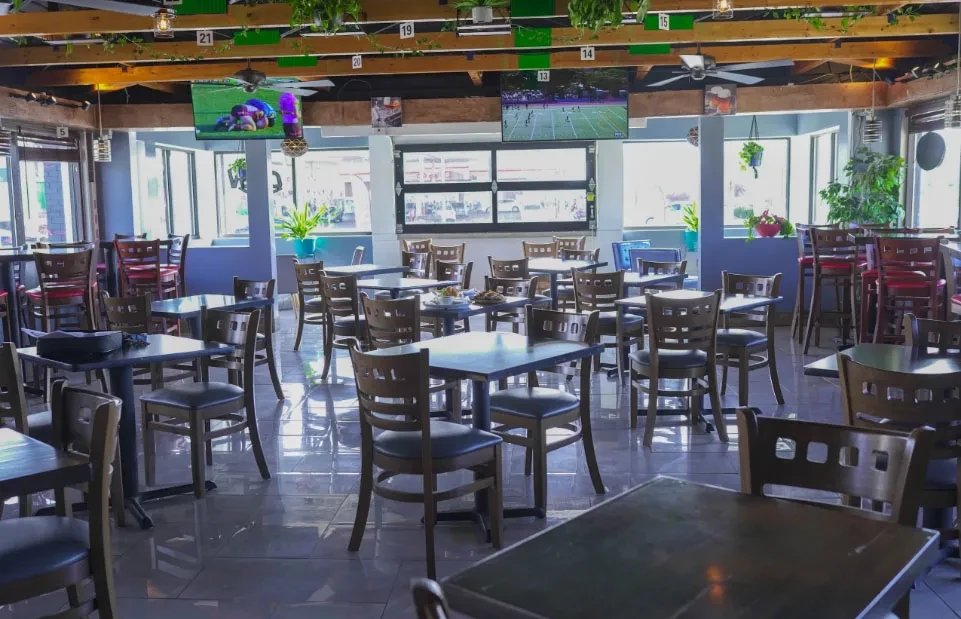 Empty, bright sports bar with tables, sports on TVs, and plants.