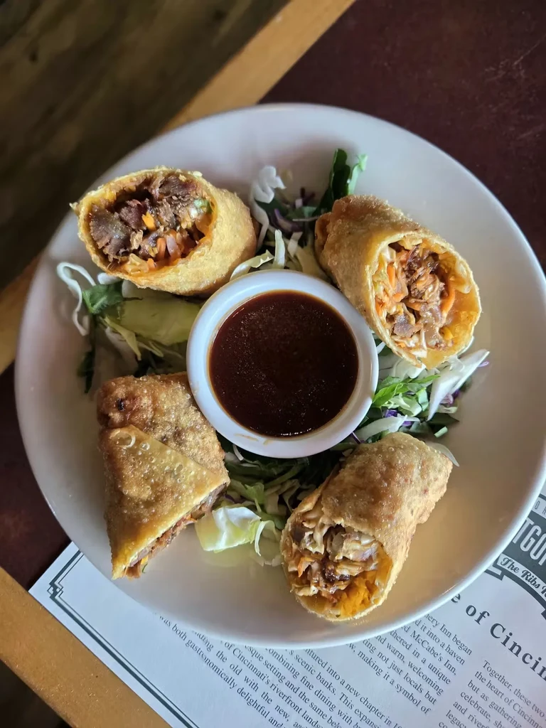 Four egg rolls, three sliced, revealing filling, with sauce and cabbage.