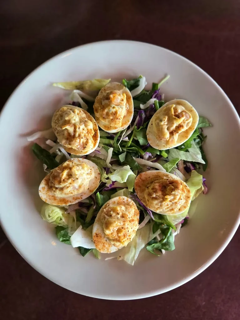 Six deviled eggs with paprika on mixed greens in a white bowl.