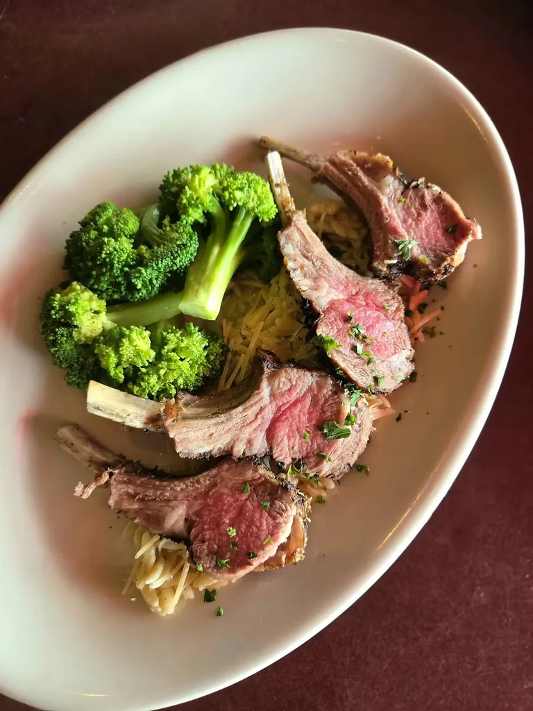 Four medium-rare lamb chops on orzo with broccoli.