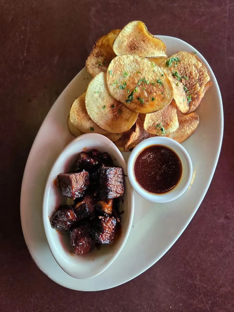 Overhead view of chips, braised meat, and dark dipping sauce.