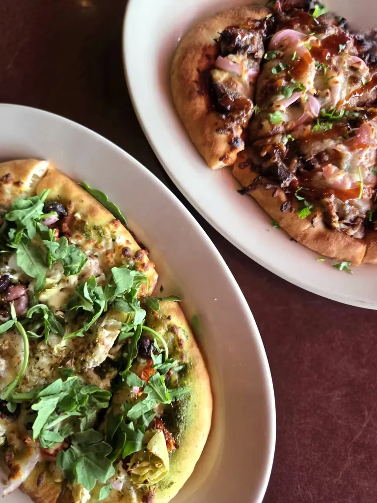 Two flatbreads: green pesto with arugula, and BBQ meat with cilantro.