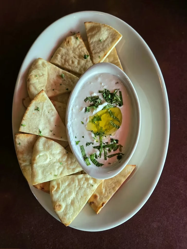 Plate of toasted pita triangles around herbed hummus with olive oil.
