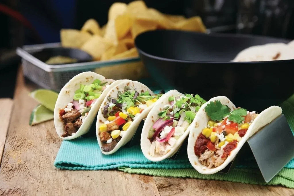 Four colorful gourmet tacos with diverse fillings, lime, on wood.