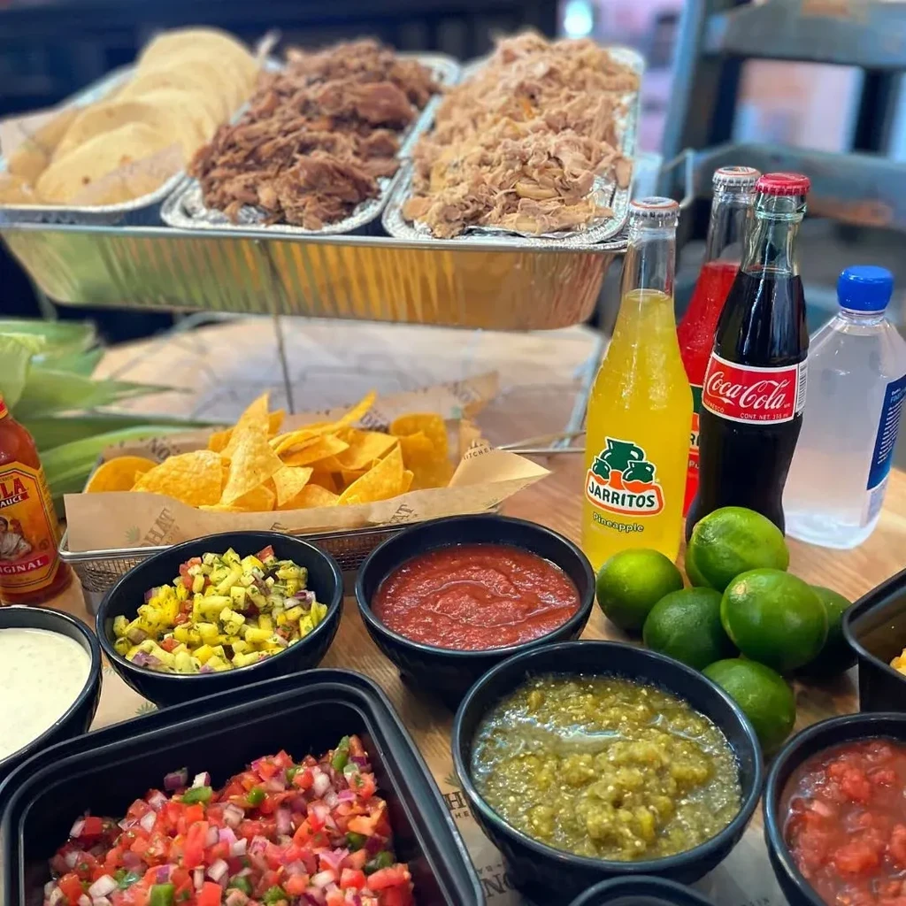 Colorful Mexican taco bar with meats, tortillas, salsas, chips, and drinks.