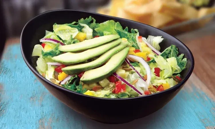 Vibrant salad with avocado, peppers, and seeds on rustic wood.