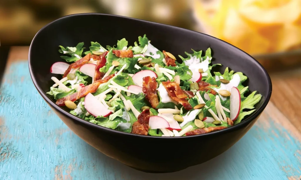Salad with lettuce, radishes, cheese, bacon, pumpkin seeds, and dressing.