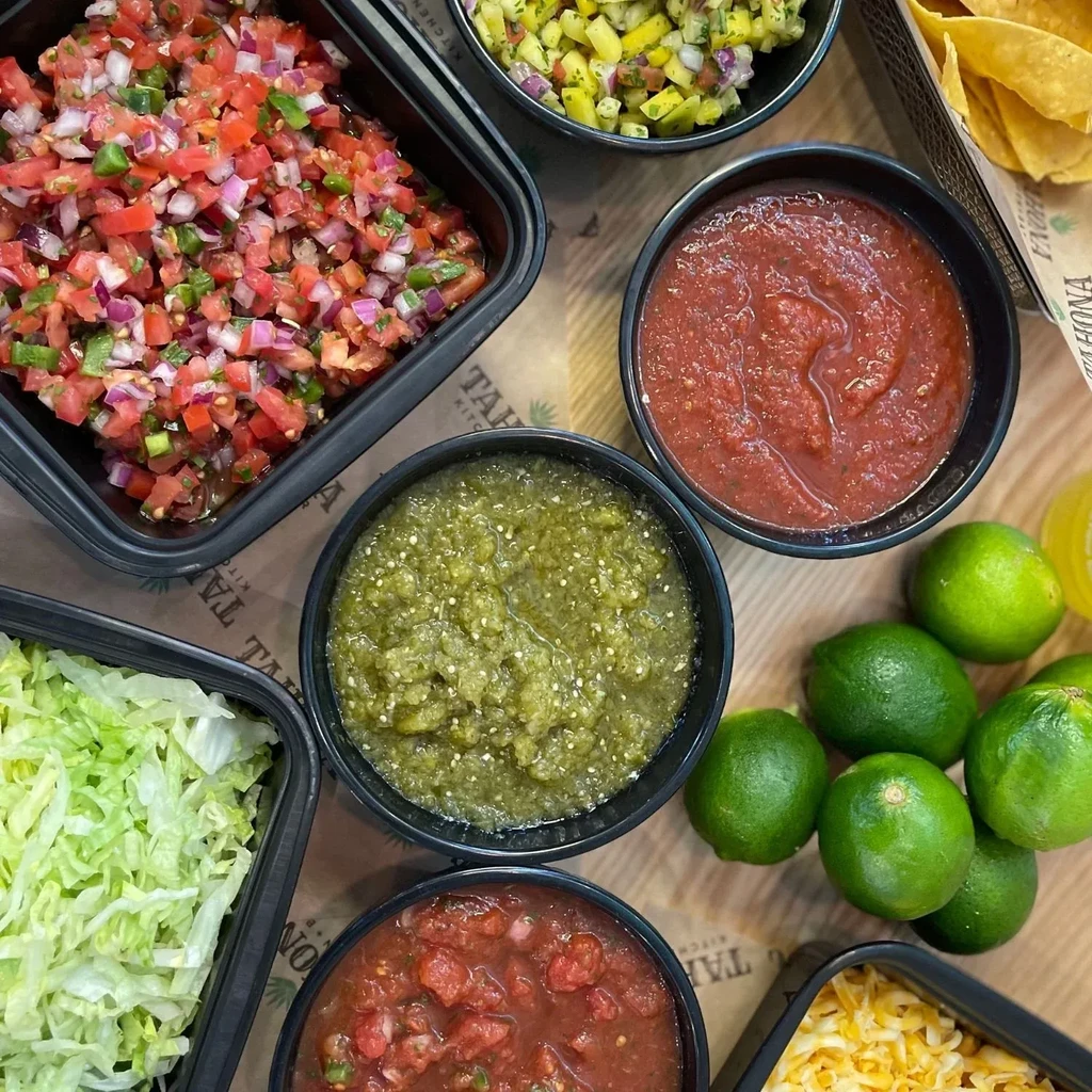 Assortment of Tahona Kitchen salsas, chips, lettuce, and fresh limes.