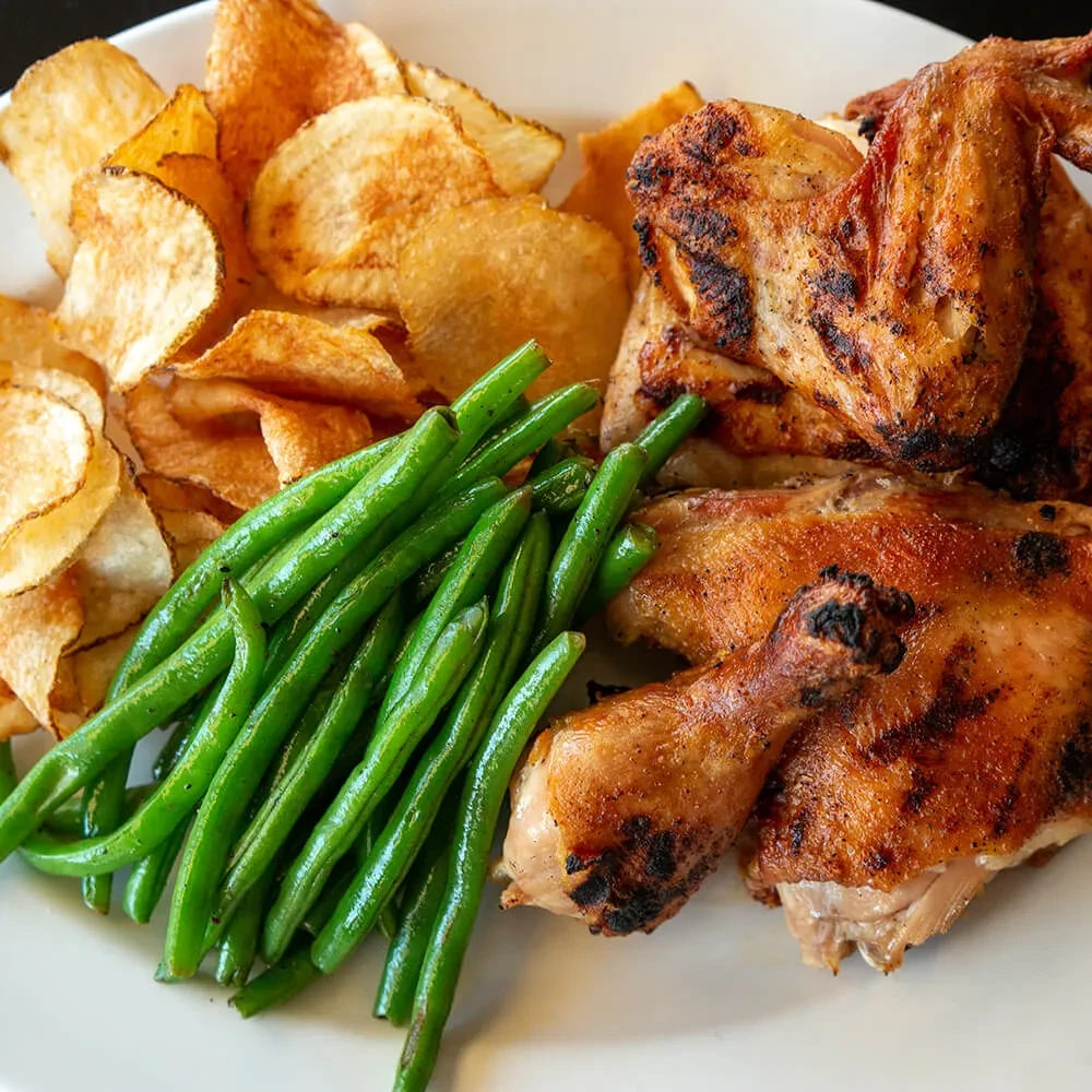 White plate with crispy chicken, green beans, and rustic potato chips.