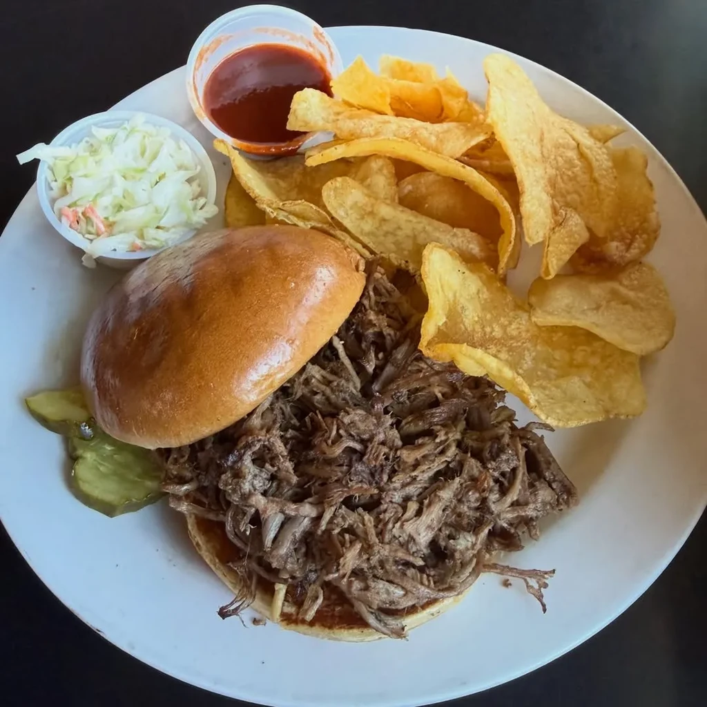 Pulled pork sandwich with chips, coleslaw, barbecue sauce, and pickles.