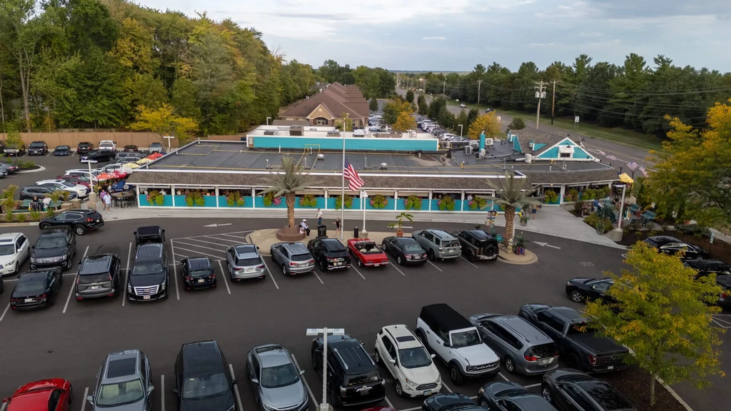 Aerial view: busy restaurant, full parking, turquoise accents, American flag, woods.