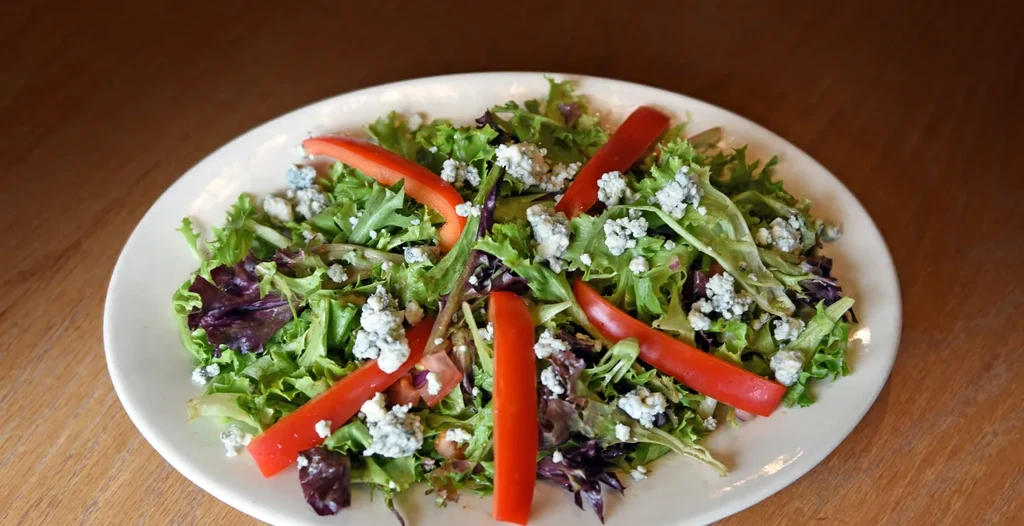 Green salad with blue cheese, red bell pepper, on plate, wooden table.