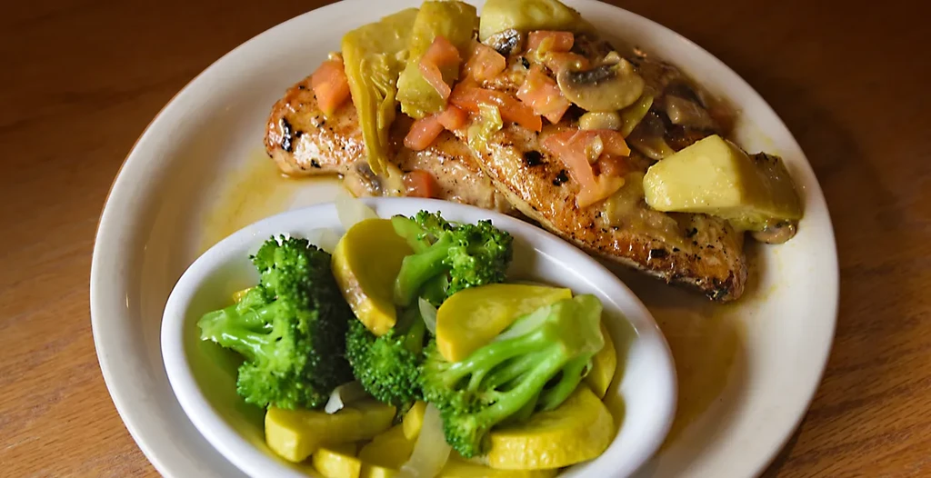 Grilled chicken with artichokes, tomatoes, and mushrooms, served with broccoli and squash.