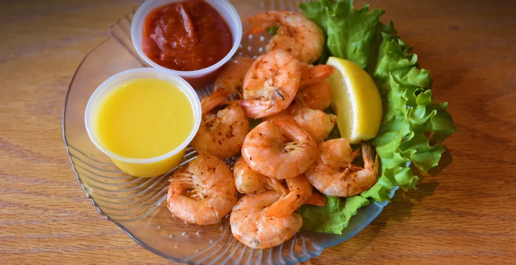 Shelled cooked shrimp on lettuce with lemon, cocktail sauce, and butter.