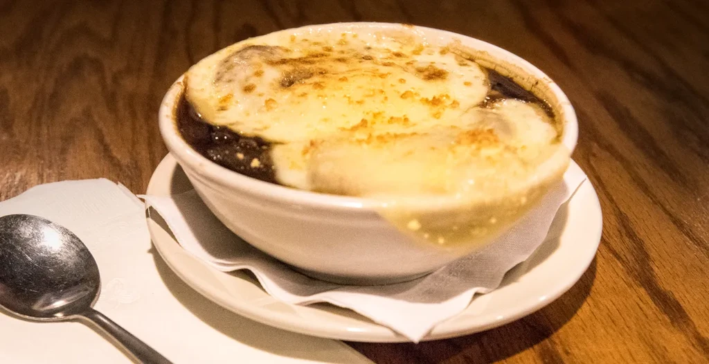 French onion soup with bubbling golden cheese, white bowl, wooden table.