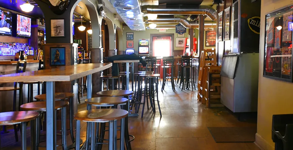Interior of an empty, rustic-industrial bar with a stocked bar and TVs.