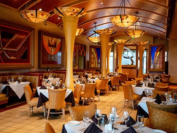 Elegant restaurant dining room with set tables, columns, and chandeliers.