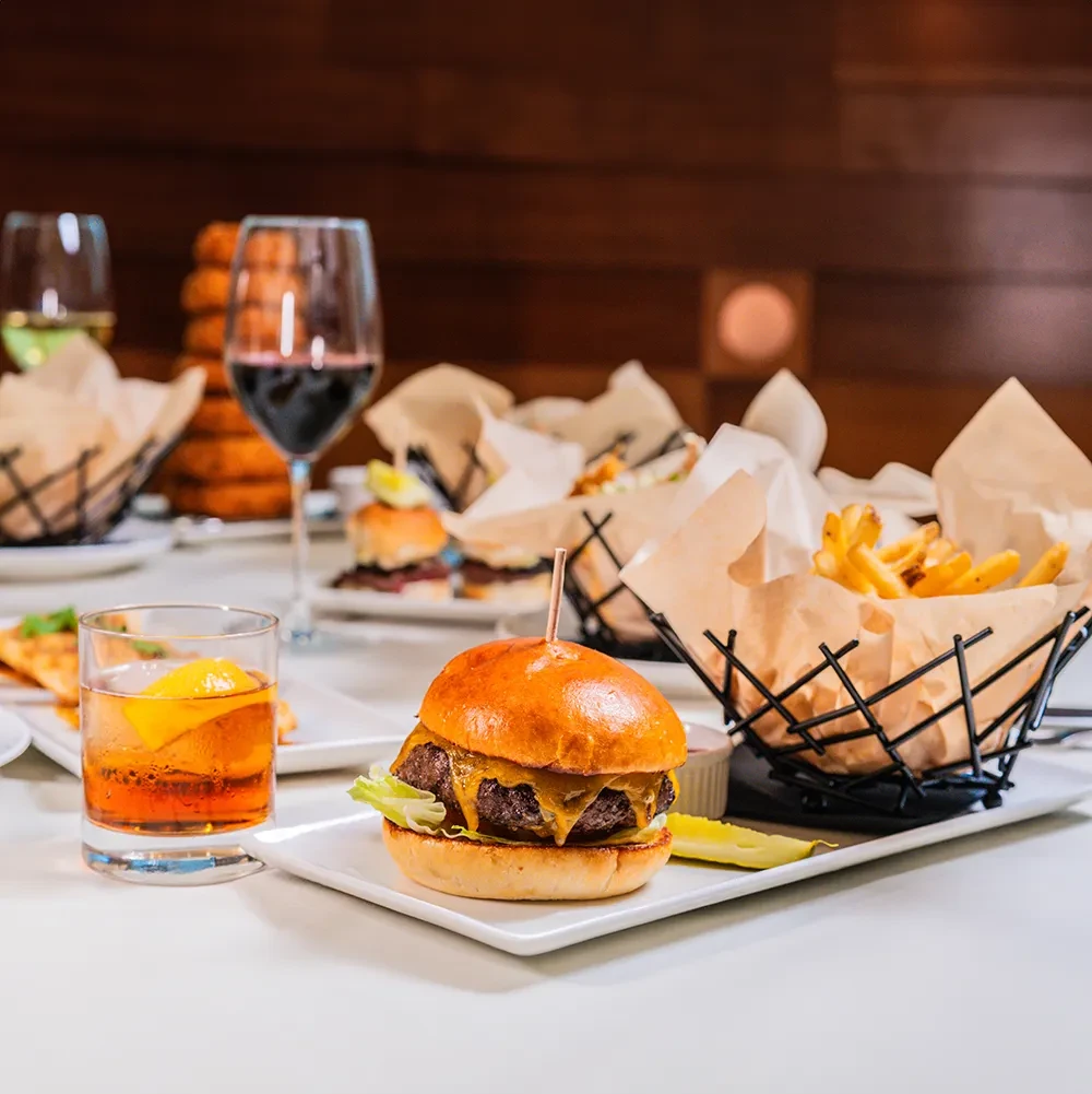 Cheeseburger, fries, pickle, and cocktail on a restaurant table.
