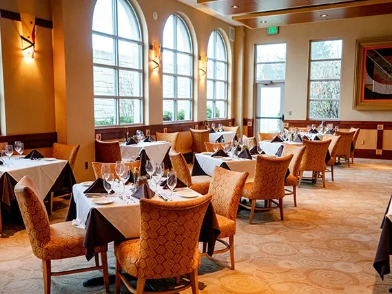 Empty, upscale restaurant dining room with set tables and arched windows.
