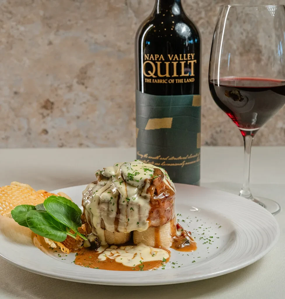 Plated meat with creamy sauce, herbs, and Napa Valley Quilt wine.