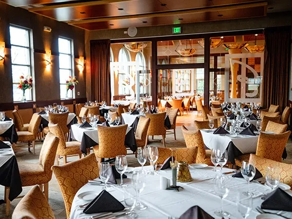 Empty upscale restaurant dining room, set tables, warm brown and gold tones.