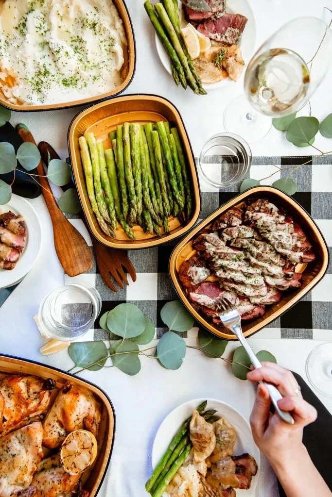 Flat lay of diverse meal: roast beef, chicken, asparagus, potatoes, wine.