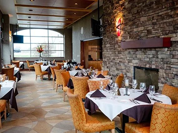 Modern restaurant interior with set tables, stone fireplace, and large arched window.