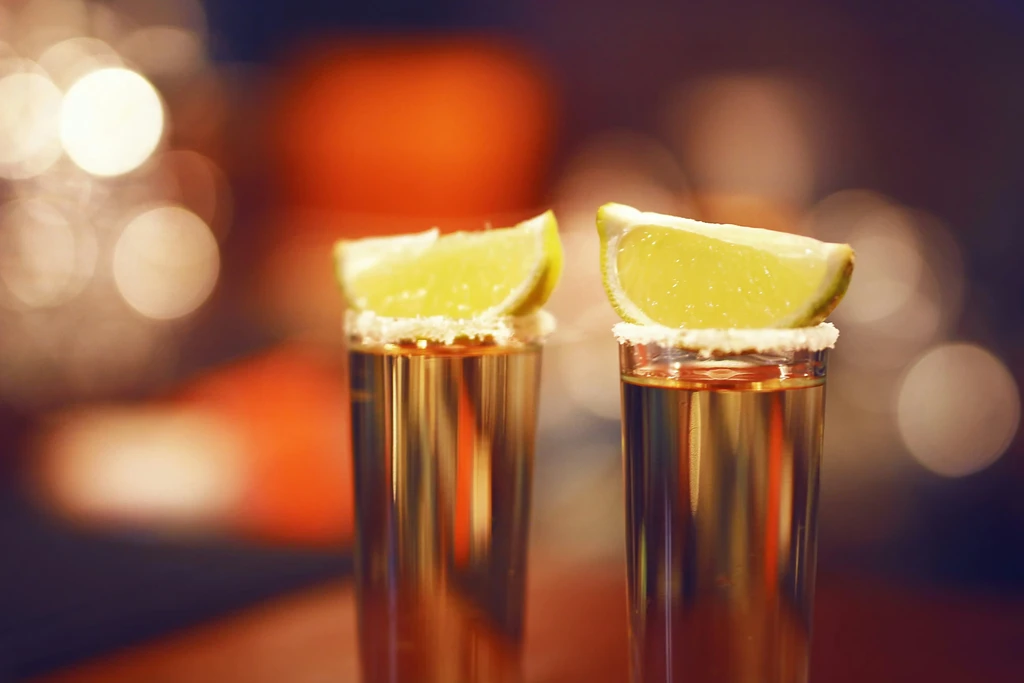 Two salt-rimmed tequila shots with lime, warm bokeh background.