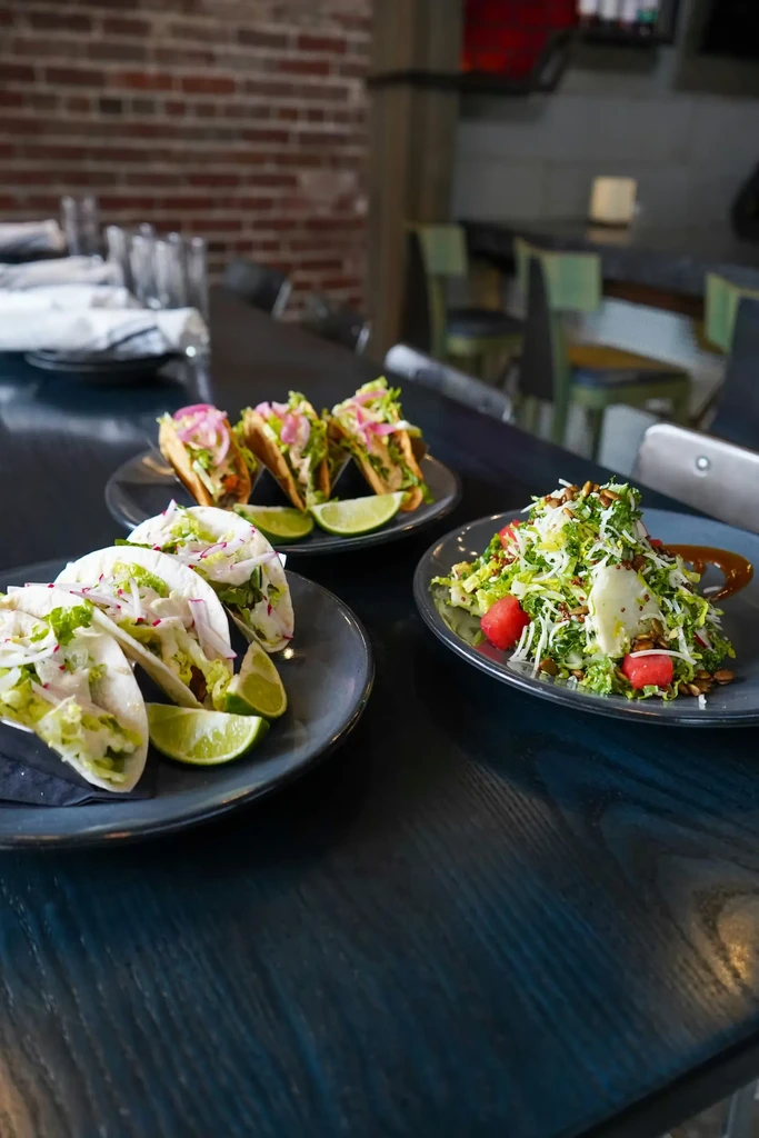 Plates of colorful tacos and a fresh salad on a restaurant table.
