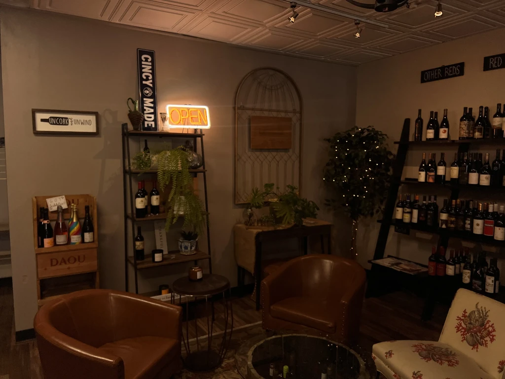 Warmly lit wine bar interior displaying wine bottles, plants, and armchairs.