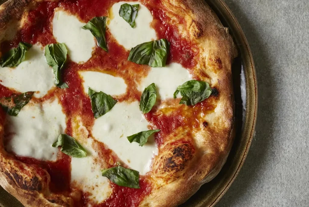 Overhead Neapolitan Margherita pizza with bubbly crust, melted mozzarella, basil.